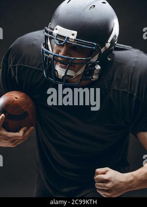 Stattlichen kaukasischen Mann mit American Football uniform und Helm in Aktion läuft mit einer Kugel über dunklen Hintergrund Stockfoto