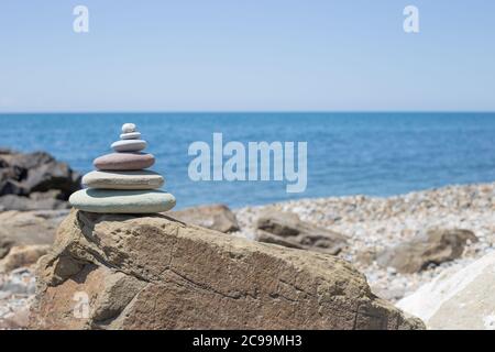 Steinen Pyramide auf Sand als Symbol für Zen, Harmonie und Balance. Meer bei Sonnenuntergang im Hintergrund Stockfoto