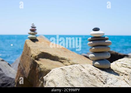 Steinen Pyramide auf Sand als Symbol für Zen, Harmonie und Balance. Meer bei Sonnenuntergang im Hintergrund Stockfoto