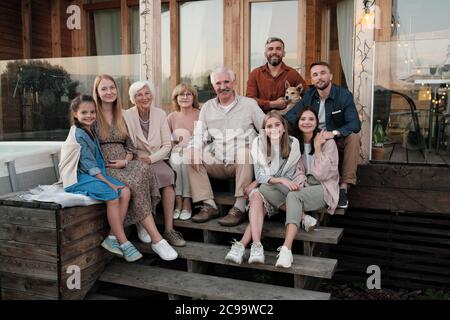 Porträt einer großen glücklichen Familie auf der Veranda sitzen und lächeln an der Kamera versammelten sie sich in ihrem großen Haus auf dem Land Stockfoto