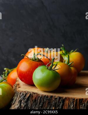 Vertikale Nahaufnahme von grünen und roten Tomaten auf einem Baumstumpf auf schwarzem Hintergrund Stockfoto