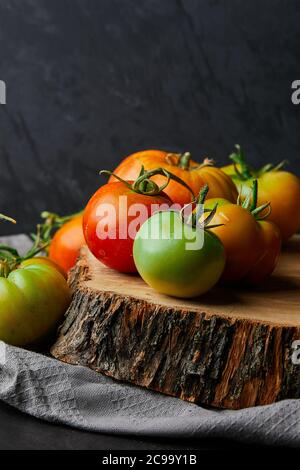 Vertikale Nahaufnahme von frischen grünen und roten Tomaten auf Ein Baumstumpf auf schwarzem Hintergrund Stockfoto