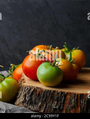 Vertikale Nahaufnahme von grünen und roten Tomaten auf einem Baumstumpf auf schwarzem Hintergrund Stockfoto
