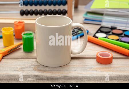 Milchbecher weiß, leer und Schulbedarf auf Holzschreibtisch Hintergrund. Getränk für Kinder Frühstück am Morgen zu Hause oder während des Studiums Hausaufgaben Stockfoto