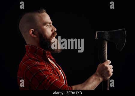 Ernsthafte Holzfäller. Zuversichtlich bärtiger Mann betrachten ax auf schwarzem Hintergrund Stockfoto