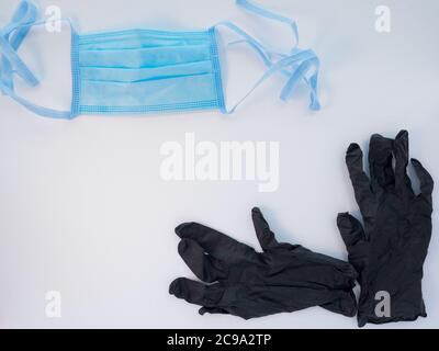Blaue schützende medizinische Gesichtsmaske und ein Paar schwarze Latexhandschuhe auf weißem Hintergrund. Antiviraler Schutz während einer Coronavirus-Pandemie. Textbereich. Stockfoto