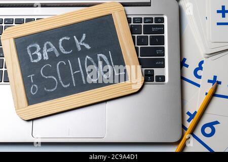 Zurück in die Schule geschrieben in Kreide auf einer kleinen Tafel auf einem Laptop-Computer mit einem gelben Bleistift und Karteikarten für das Konzept der alten Schule ve Stockfoto