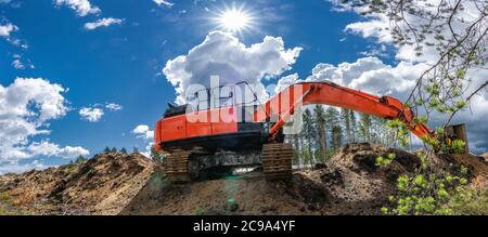 Orange Bagger hinter den Kiefernästen steht auf der Oberseite von Graben Sand gegraben. Voll gestreckten Arm mit Eimer liegt entlang der Schmutz in der Nähe t Stockfoto