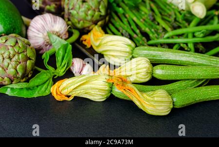 Zucchini mit Blumen und Vielfalt von grünem Gemüse auf dunklem Hintergrund, kopieren Raum Stockfoto