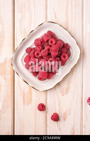 Himbeerfrüchte in weißem Teller, gesunder Stapel Sommerbeeren auf Holzgrund, Draufsicht Stockfoto