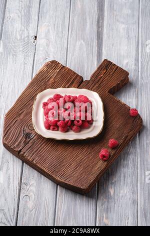 Himbeerfrüchte in Teller auf altem Teakholz Schneidebrett, gesunder Stapel Sommerbeeren auf Holzhintergrund, Winkelansicht Stockfoto