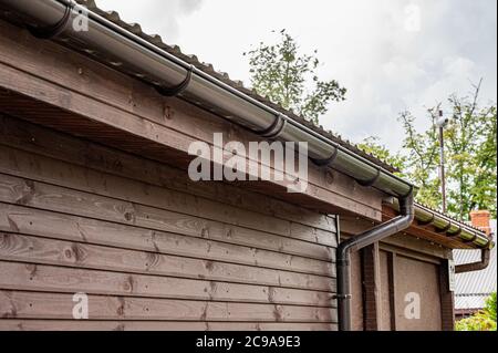 Dachkante eines kleinen Hauses mit installiertem Regenwasser-Abflusssystem. Regenrinnenanlage. Stockfoto