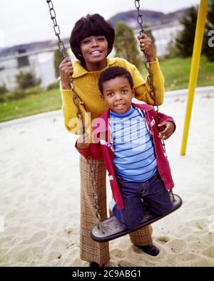 1970S AFRICAN-AMERICAN FRAU MUTTER HINTER IHREM SOHN JUNGE KNIET AUF SPIELPLATZ SCHAUKEL BLICK AUF KAMERA BEIDE LÄCHELND - KJ5363 PHT001 HARS PAAR VORSTADTFARBE IHRE MÜTTER ALTE ZEIT NOSTALGIE ALTE MODE 1 FITNESS JUGENDLICH STIL GESUNDE JUNGE ERWACHSENE SICHERHEIT STARKE SÖHNE FREUDE LIFESTYLE FRAUEN ZU HAUSE LEBEN KOPIEREN RAUM HALB-LÄNGE DAMEN PERSONEN PFLEGE MÄNNER AUGENKONTAKT KNIEND AKTIVITÄT KÖRPERLICHE FRÖHLICH BEIDE SCHUTZ STÄRKE AFRO-AMERIKANER AFRO-AMERIKANISCHE ERHOLUNG SCHWARZE ETHNIZITÄT AUF LÄCHELT VERBINDUNG FLEXIBILITÄT FREUDIGE MUSKELN PERSÖNLICHE BINDUNG ZUNEIGUNG EMOTION JUVENILES MÜTTER Stockfoto