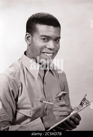 1950S 1960S AFRICAN-AMERICAN MAN WEARING WORK SHIRT HOLDING CLIPBOARD AND PENCIL SMILING LOOKING AT CAMERA - N289 HAR001 HARS KARRIERE JUNG ADULT SICHERHEIT INFORMATION FREUDE LIFESTYLE JOBS STUDIO SHOT HEALTHINESS MANAGER COPY SPACE HALF-LENGTH PERSONS CARING MÄNNLICH BERUF VERTRAUEN FÜHRUNGSKRÄFTE AUSDRÜCKE B&W BLICKKONTAKT GESCHICKLICHKEIT BERUF GLÜCK FÄHIGKEITEN FRÖHLICH STÄRKE STRATEGIE AFROAMERIKANER AFROAMERIKANER UND KARRIEREN FÜHRUNG SCHWARZE ETHNIZITÄT RICHTUNG ARBEIT STOLZ GELEGENHEIT AUTORITÄT BESCHÄFTIGUNG BERUFE LÄCHELT CHEFS KONZEPTIONELL FRÖHLICH STILVOLLE MITARBEITER MANAGER PRÄZISION Stockfoto