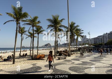 RIO DE JANEIRO, BRASILIEN - 19. Jul 2020: Frau in Gesichtsmaske flaniert entlang Copacabana Boulevard mit Palmen flankieren den Strand im Hintergrund Stockfoto