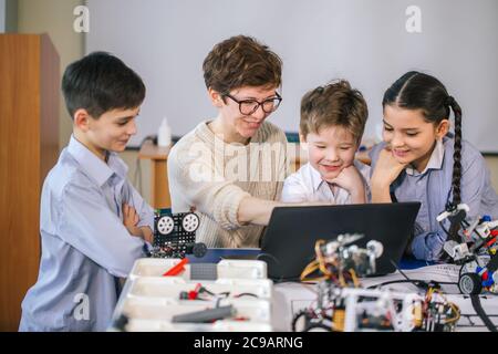 Gruppe von Happy Kids mit ihren weiblichen Erwachsenen Wissenschaft prof mit Tablet-PC Computer Programmierung elektrische Spielzeuge und Roboter Robotik Hobby Club Stockfoto