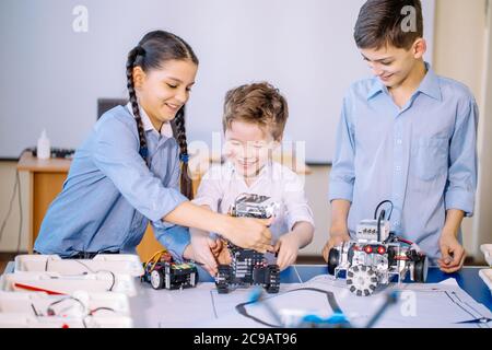 Kleines Kind und zwei lächelnde jugendlich Freunde Roboter Spielzeug beim Spielen in ihrer Freizeit in der technischen Werkstatt konstruieren aufgeregt. Intelligente Acti Stockfoto