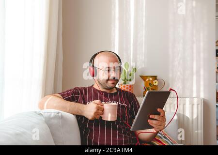 Junge Leute haben eine gute Zeit zu Hause. Musik hören, Kaffee und Tee trinken. Ruhender Teenager läuft mit Tablet und Leptop in den Händen. Stockfoto