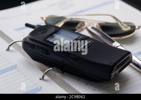 Neunzigs Handy, ein silberner Füllfederhalter und ein Paar Sonnenbrillen sitzen auf einem großformatigen Tagebuch. Stockfoto