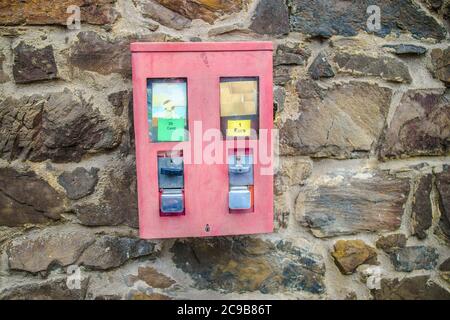 Rote Gummiballmaschine, die an einer Ziegelwand-Fassade hängt Stockfoto