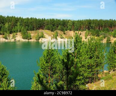 Ein Fragment eines schönen Sees mit klarem smaragdgrünen Wasser, umgeben von einem Pinienwald an hohen Ufern. Marmorsee im Dorf Abrashino, Novosibir Stockfoto