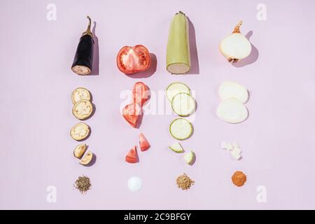 Scheiben von Gemüse Reihen Tomaten, Kürbis, Auberginen, Zwiebeln und Gewürze auf rosa Hintergrund. Kochen Gemüseeintopf. Stockfoto