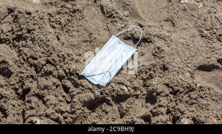 Travemünde, Schleswig-Holstein / Deutschland - 24. Juni 2020: Nahaufnahme einer Einweg-OP-Maske am Sandstrand. Teil der 'Neuen Normalität' Stockfoto