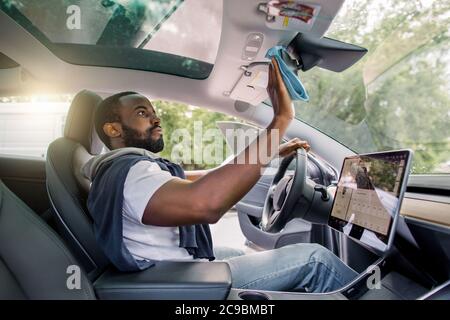 Professioneller afrikanischer Mann, Autobesitzer oder Servicemitarbeiter, Reinigung Auto Interieur, Auto Spiegel mit Mikrofaser Kleidung. Details zum Fahrzeug. Modern futuristisch Stockfoto