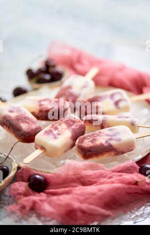 Hausgemachte vegane Kirschpopsicles mit Kokosmilch. Platziert auf Keramikplatte Stockfoto