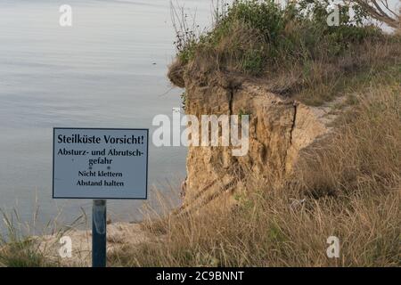 Weißes Warnschild mit Inschrift auf Deutsch - Vorsicht vor Klippen an der Ostsee auf dem Darss Stockfoto