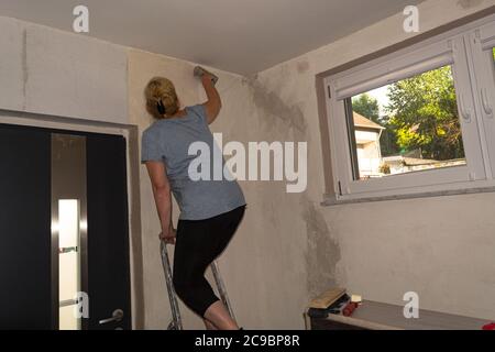 Frau in legerer Kleidung, Tapetenrollen an der Wand. Instrumente, Zubehör, Werkzeuge für die Renovierung Gehäuse. Reparatur Home Konzept Stockfoto