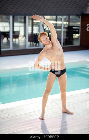Junger lächelnder Kerl, der sich neben dem Pool lehnte Stockfoto