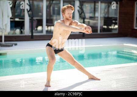 Barfuß Mann im Badeanzug, der Muskeln in der Nähe des Pools beugend Stockfoto