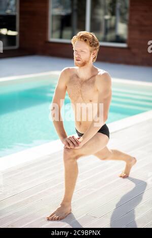 Rothaariger Mann, der in der Nähe des Pools Schritt und Ausfallschritt Stockfoto