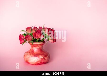 Seitenansicht des minimalistischen zarten kleinen rosa Rosenblütenbuketts in kleiner Keramikvase auf pastellfarbenem Hintergrund. Flaches Lay Vintage Retro stilvoll handgefertigt Stockfoto