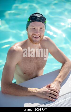 Lächelnder Schwimmer, der im Wasser am Rand des Pools steht Stockfoto