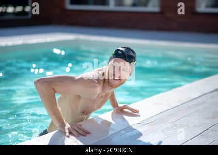 Lächelnder Mann im Pool schaut seitwärts interessiert Stockfoto