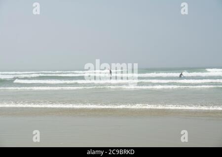 Zwei Surfer im Meer in Tofino, BC, am Cox Bay Beach an einem nebligen Tag. Auf Vancouver Island an der kanadischen Westküste. Stockfoto