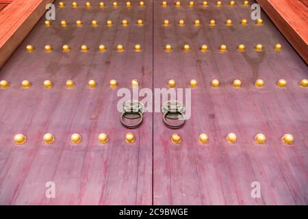 Rote chinesische Holztür mit Metall Klopfer und goldenen Klopfer Nägel in Peking, China Stockfoto