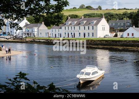 Kleines weißes Motorboot, das in Cushendun in der Grafschaft Antrim Nordirland festgemacht ist, mit dem Glendun River und dem Cushendun Hotel im Hintergrund. Stockfoto