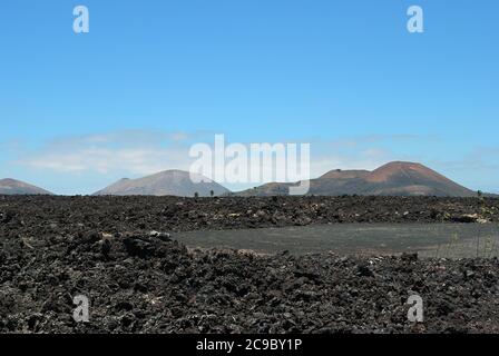 Die weite Leere und Einsamkeit der Lanzarote schwarz gefrorenen Lava vulkanischen Wüste und Vulkane im Hintergrund. Lanzarote, Kanarische Inseln. Spanien Stockfoto