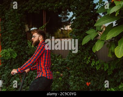 Hübscher junger bärtiger Kaukasusmann mit Sonnenbrille reitet auf dem Street e Scooter Stockfoto