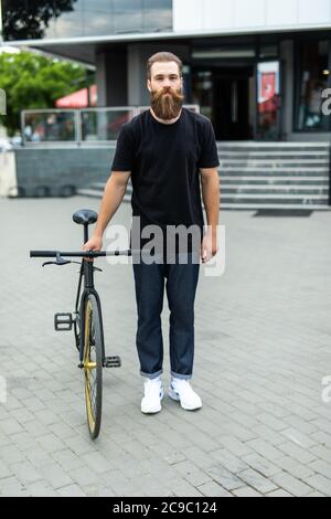 Selbstbewussten jungen bärtigen Mann freuen uns auf dem Fahrrad entlang der Straße Stockfoto