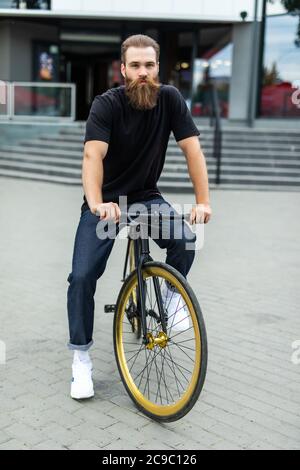 Genießen Sie seine Fahrt. Selbstbewusster junger bärtiger Mann, der sich auf seinem Fahrrad auf der Straße freut Stockfoto