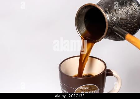 Schwarzer Kaffee am Morgen. Der Prozess der Ausgießung Espresso, americano aus Kupfer türke in eine Kaffeetasse. Stockfoto