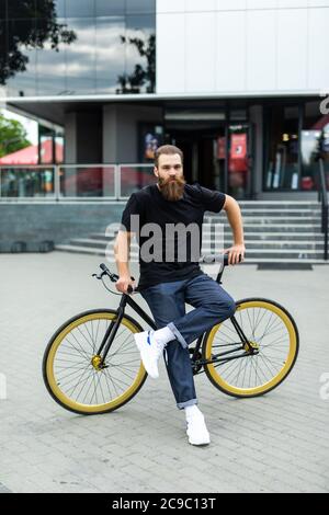 Selbstbewussten jungen bärtigen Mann freuen uns auf dem Fahrrad entlang der Straße Stockfoto