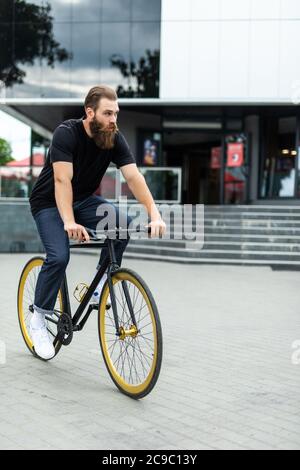 Genießen Sie seine Fahrt. Selbstbewusster junger bärtiger Mann, der sich auf seinem Fahrrad auf der Straße freut Stockfoto
