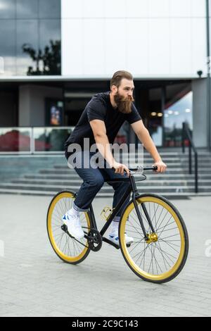 Selbstbewussten jungen bärtigen Mann freuen uns auf dem Fahrrad entlang der Straße Stockfoto