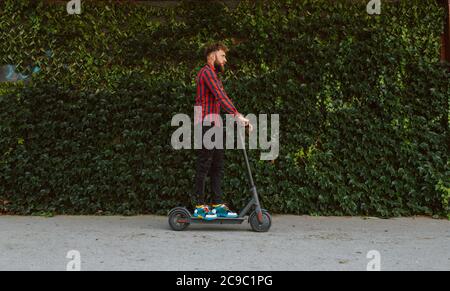 Seitenansicht eines hübschen jungen bärtigen kaukasischen Mannes mit Sonnenbrille Fahrten auf der Straße e Scooter Stockfoto