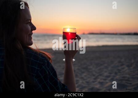 Frau mit einem Glas Wein am Strand bei Sonnenuntergang. Genießen Sie das Leben, langsam leben Stockfoto
